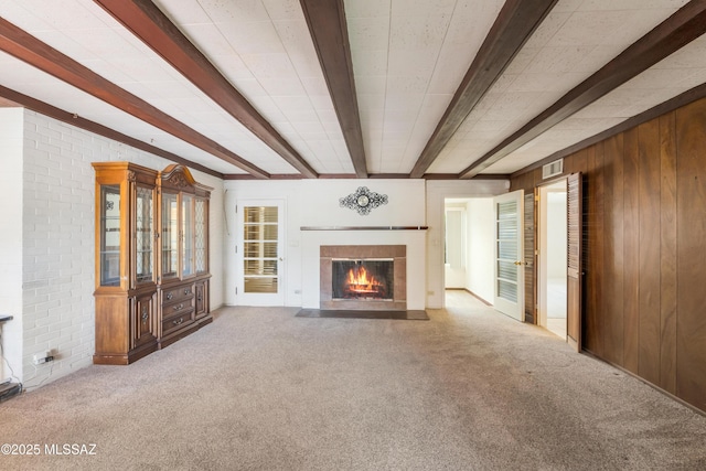 1047 E Hedrick Dr, Tucson, AZ 85719 - unfurnished living room featuring carpet, beamed ceiling, a fireplace with flush hearth, wood walls, and brick wall