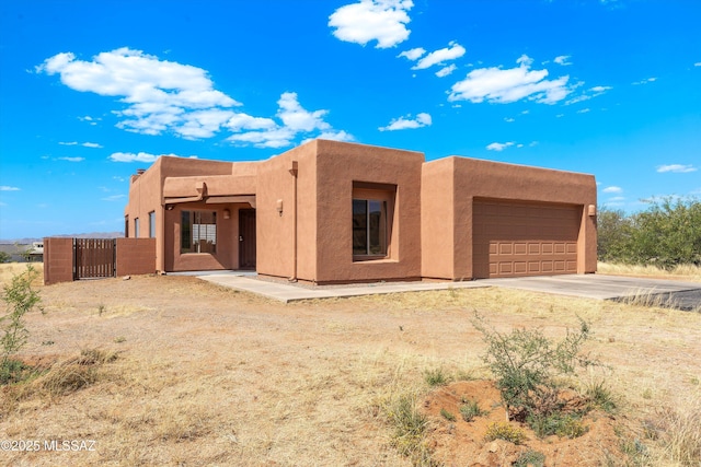 adobe home featuring an attached garage, driveway, stucco siding, and a gate