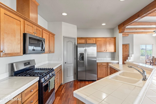 kitchen featuring stainless steel appliances, a sink, tile countertops, dark wood-style flooring, and recessed lighting