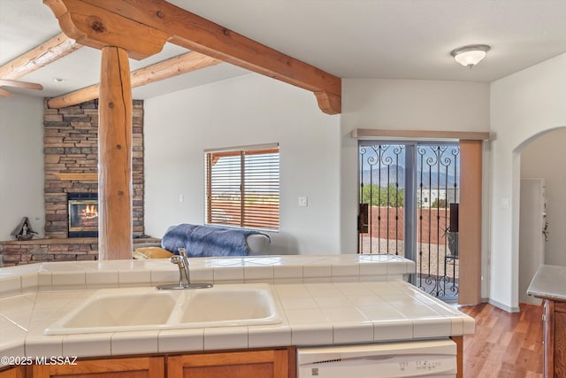 kitchen with dishwasher, a sink, beamed ceiling, tile counters, and arched walkways