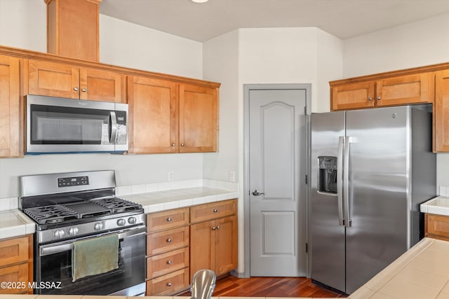 kitchen featuring appliances with stainless steel finishes, tile countertops, dark wood-type flooring, and brown cabinets