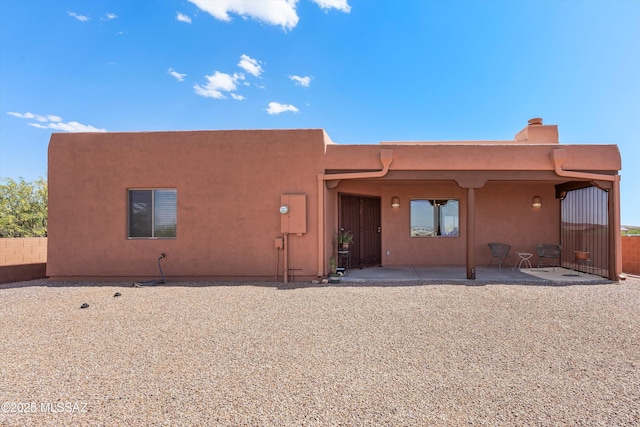 back of house featuring a patio area, stucco siding, fence, and a chimney