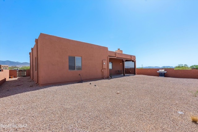 back of house featuring a fenced backyard, stucco siding, a mountain view, and a chimney