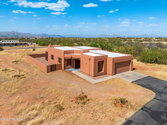 pueblo-style house featuring a mountain view, stucco siding, a garage, and asphalt driveway