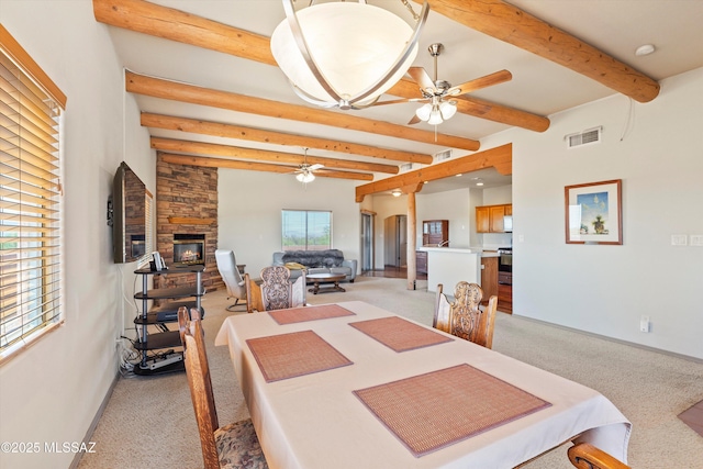 dining area with a ceiling fan, light carpet, beamed ceiling, baseboards, and a fireplace