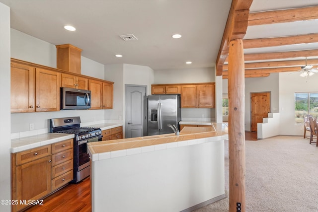 kitchen featuring stainless steel appliances, tile countertops, recessed lighting, ceiling fan, and brown cabinets