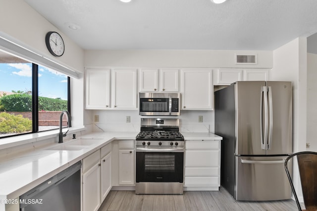 kitchen featuring a sink, stainless steel appliances, visible vents, light wood-style flooring, and white cabinetry