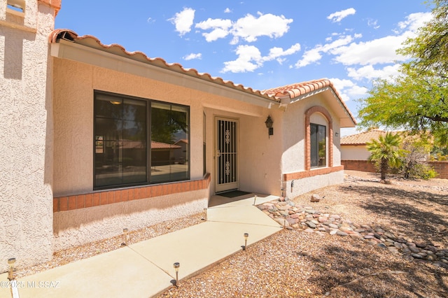view of exterior entry with fence, stucco siding, and a tiled roof