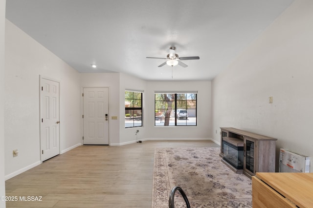 living room with baseboards, light wood-style floors, a fireplace, and ceiling fan