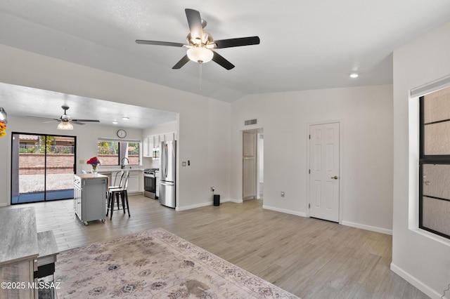 living area with vaulted ceiling, light wood-style floors, visible vents, and a ceiling fan