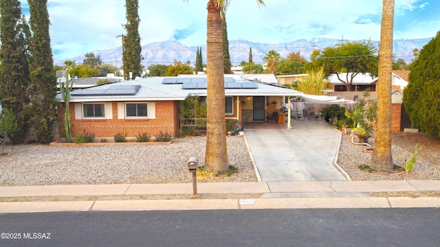 view of front of home featuring driveway, brick siding, a mountain view, a porch, and roof mounted solar panels