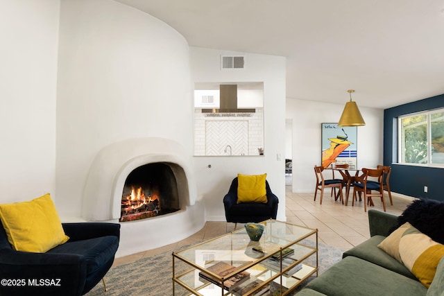 tiled living area with visible vents, a warm lit fireplace, and baseboards