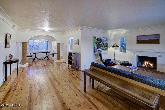 living room with baseboards, crown molding, a lit fireplace, arched walkways, and light wood-type flooring