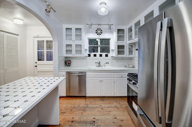 kitchen with white cabinets, tile countertops, light wood-type flooring, arched walkways, and appliances with stainless steel finishes