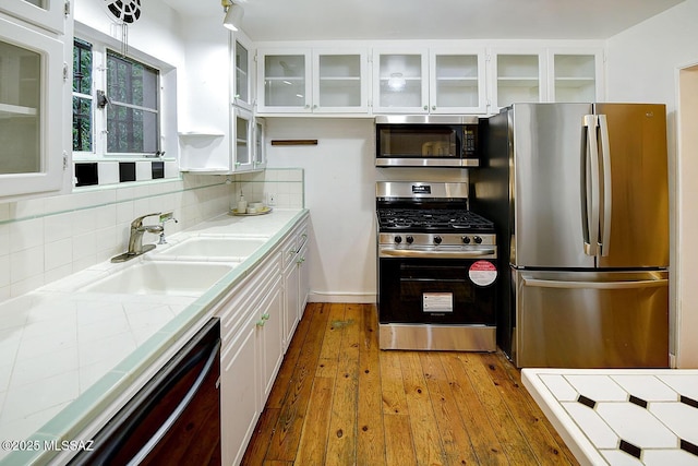 kitchen with light wood finished floors, a sink, backsplash, white cabinets, and appliances with stainless steel finishes