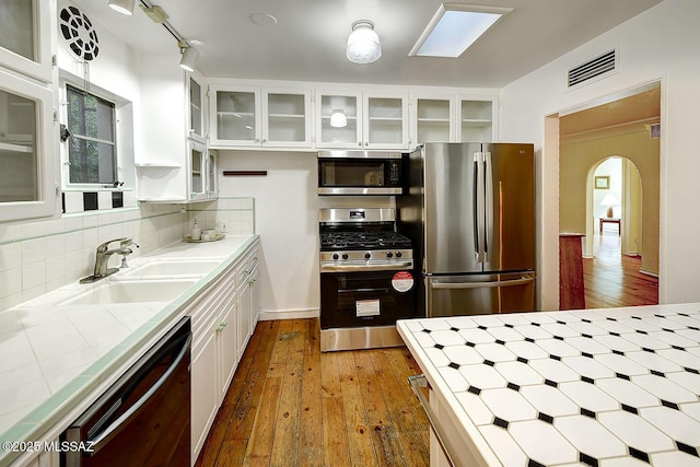 kitchen with hardwood / wood-style flooring, stainless steel appliances, visible vents, arched walkways, and tile counters