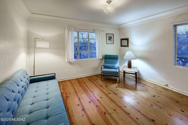 sitting room with crown molding, baseboards, wood-type flooring, and a textured wall