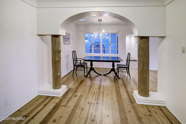 dining room with wood-type flooring, a chandelier, baseboards, and arched walkways