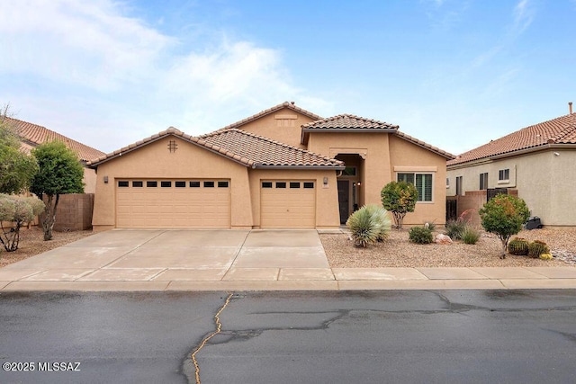 mediterranean / spanish house featuring an attached garage, stucco siding, driveway, a tiled roof, and fence
