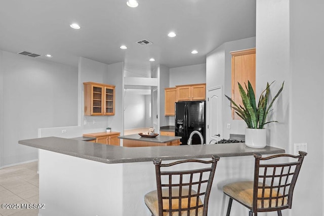 kitchen featuring black refrigerator with ice dispenser, a peninsula, recessed lighting, a center island, and dark countertops