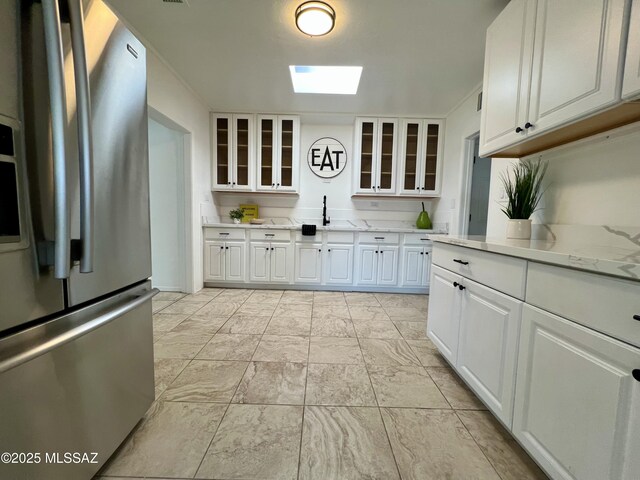 2838 E Beverly Dr, Tucson, AZ 85716 - kitchen with stainless steel fridge, a skylight, a sink, glass insert cabinets, and white cabinets