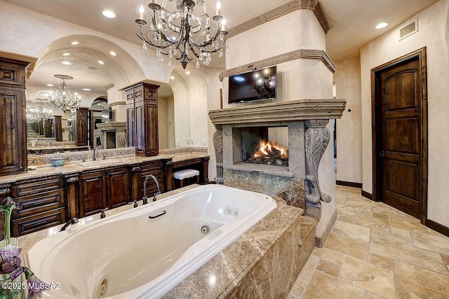 6015 N Camino Preciado, Tucson, AZ 85718 - bathroom featuring a lit fireplace, a chandelier, stone tile floors, a jetted tub, and recessed lighting