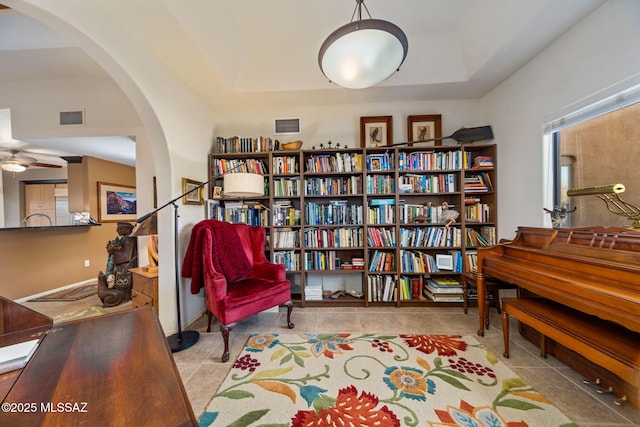 living area featuring arched walkways, tile patterned floors, a tray ceiling, and ceiling fan