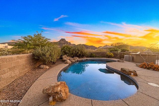 pool at dusk featuring fence and a mountain view