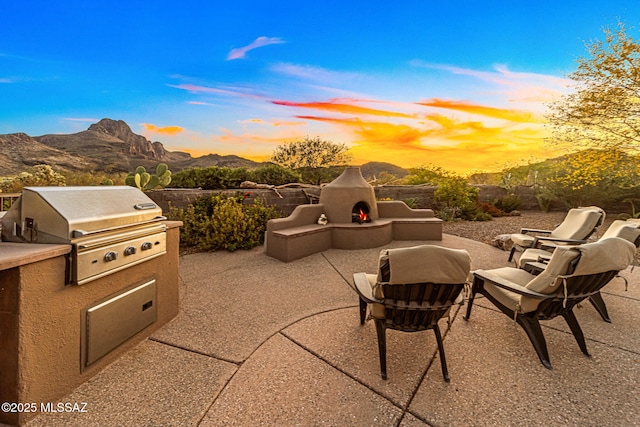 view of patio featuring a warm lit fireplace, area for grilling, exterior kitchen, and a mountain view