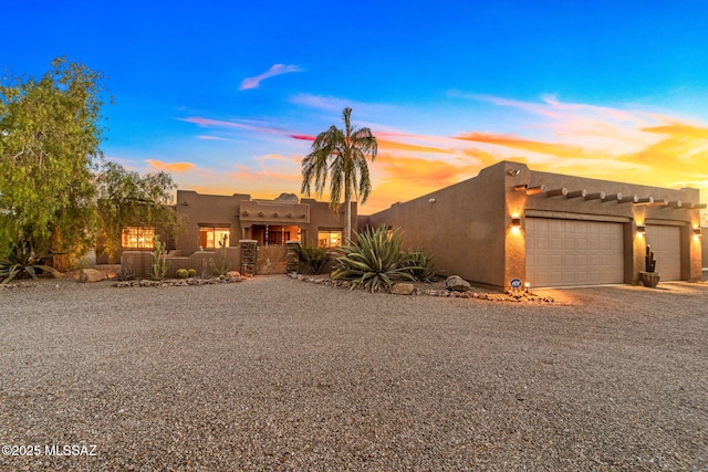 pueblo revival-style home with a garage, gravel driveway, and stucco siding