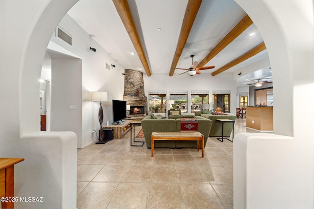 living area with a ceiling fan, beamed ceiling, light tile patterned flooring, a fireplace, and arched walkways
