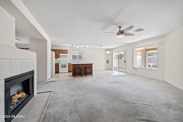 9410 E Grapevine Spring Pl, Tucson, AZ 85710 - living area featuring a tiled fireplace, visible vents, ceiling fan, track lighting, and light colored carpet
