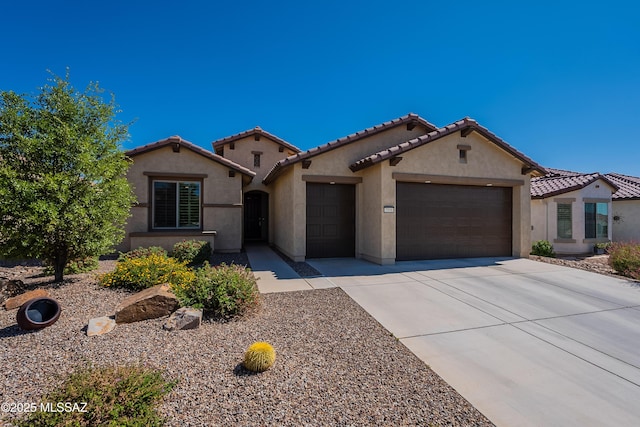 mediterranean / spanish house with an attached garage, driveway, stucco siding, and a tile roof