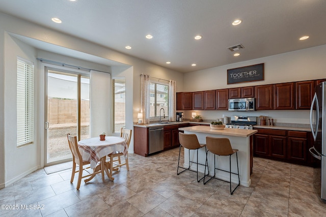 kitchen with appliances with stainless steel finishes, a sink, a center island, light countertops, and a kitchen bar
