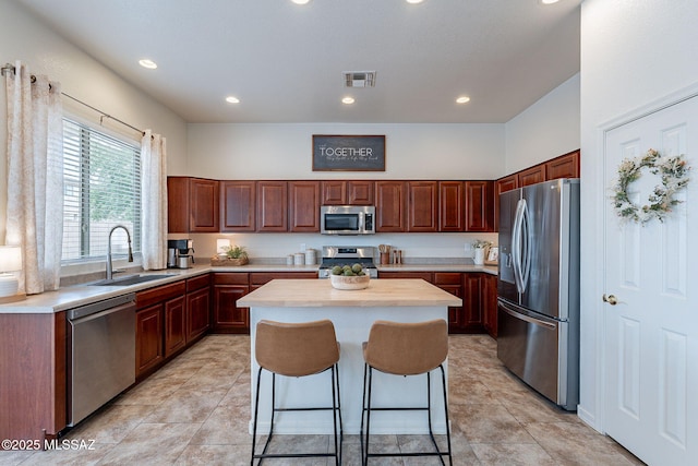 kitchen featuring stainless steel appliances, a sink, light countertops, a center island, and recessed lighting