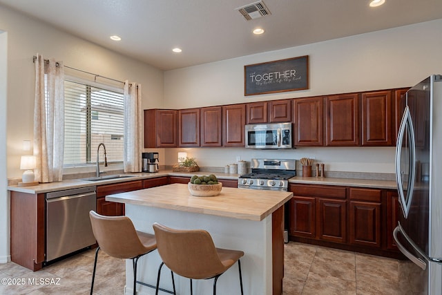 kitchen with appliances with stainless steel finishes, a sink, a breakfast bar area, butcher block counters, and a center island