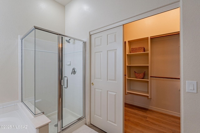 full bathroom with a shower stall, a walk in closet, wood finished floors, and a bath