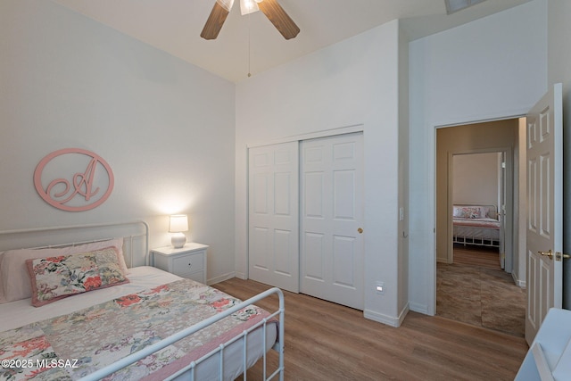 bedroom featuring light wood-type flooring, a closet, baseboards, a high ceiling, and ceiling fan