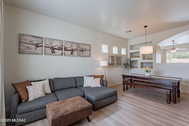living area featuring wood finished floors, arched walkways, baseboards, and a ceiling fan