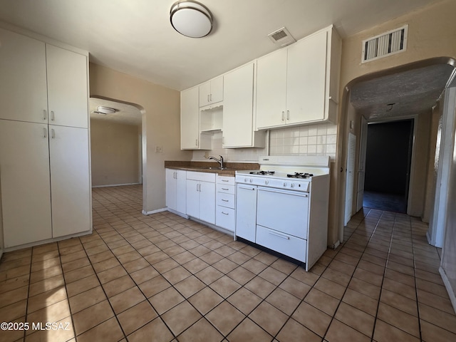 3638 S Bronson Ave, Tucson, AZ 85713 - kitchen with white gas range, arched walkways, backsplash, white cabinets, and light tile patterned floors
