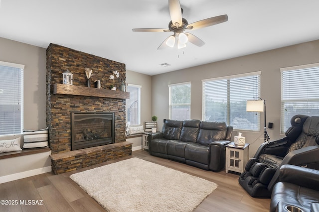 3443 W Tailfeather Dr, Marana, AZ 85658 - living room featuring a stone fireplace, light wood finished floors, a ceiling fan, and baseboards