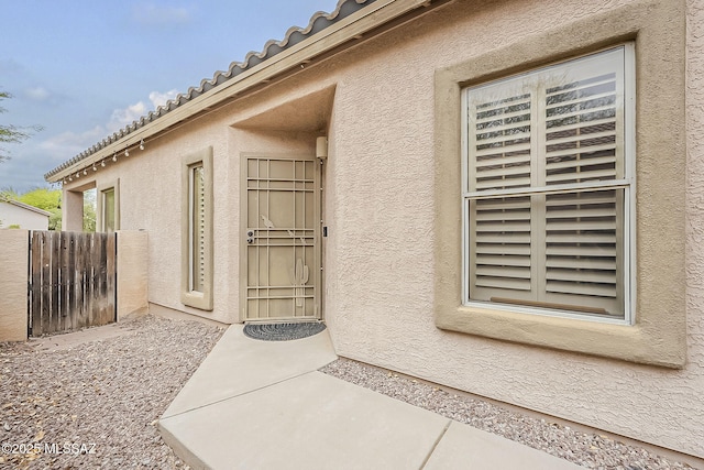 entrance to property featuring stucco siding and fence