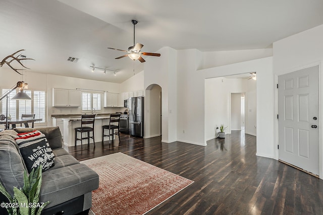 living area featuring ceiling fan, arched walkways, dark wood finished floors, baseboards, and high vaulted ceiling