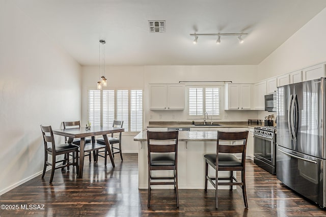 kitchen featuring appliances with stainless steel finishes, a sink, dark wood-style flooring, and a breakfast bar