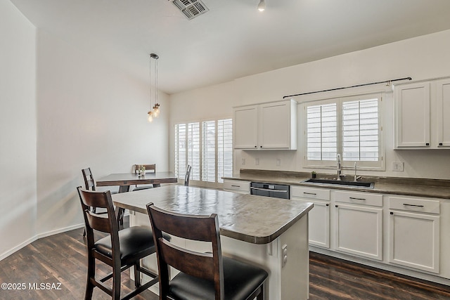 kitchen with a sink, dark wood-type flooring, dark countertops, a kitchen bar, and white cabinets