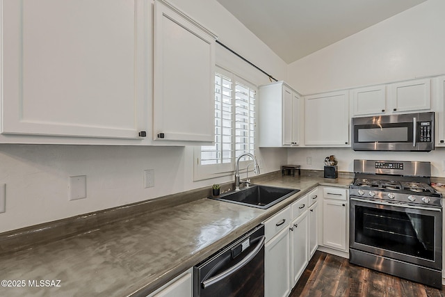 kitchen featuring stainless steel appliances, a sink, vaulted ceiling, white cabinets, and dark wood-type flooring
