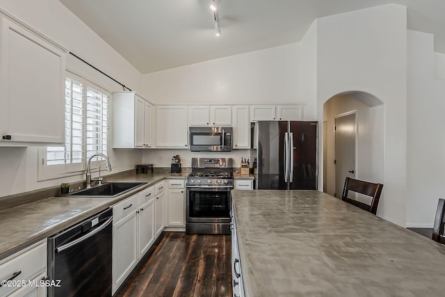 kitchen featuring appliances with stainless steel finishes, a sink, arched walkways, dark wood finished floors, and white cabinetry