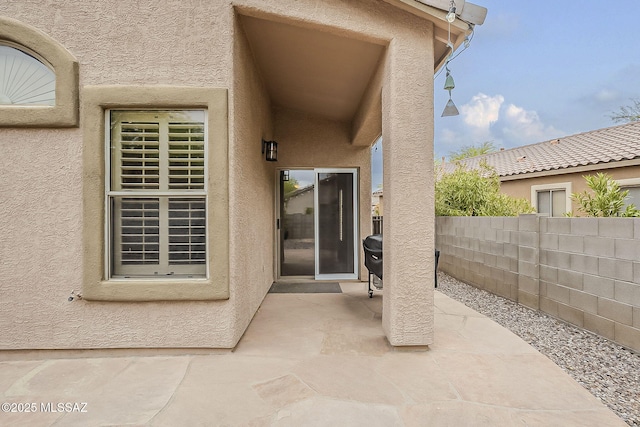 view of exterior entry with a patio, stucco siding, and fence