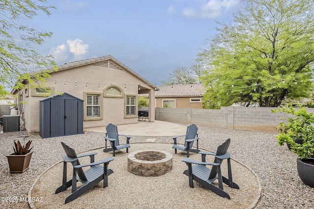 view of patio featuring an outdoor fire pit, central AC, a storage shed, a fenced backyard, and an outbuilding
