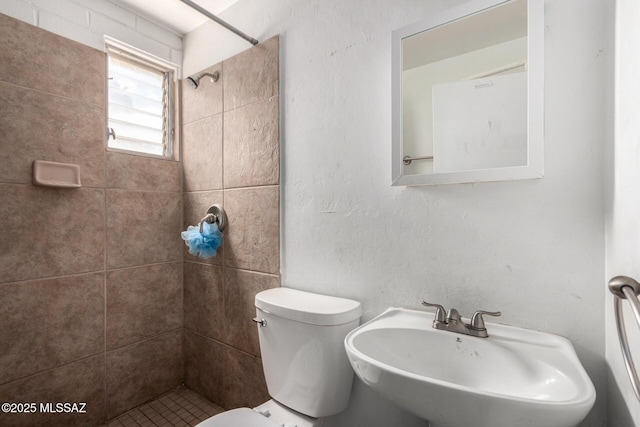 full bathroom featuring toilet, a tile shower, and a sink